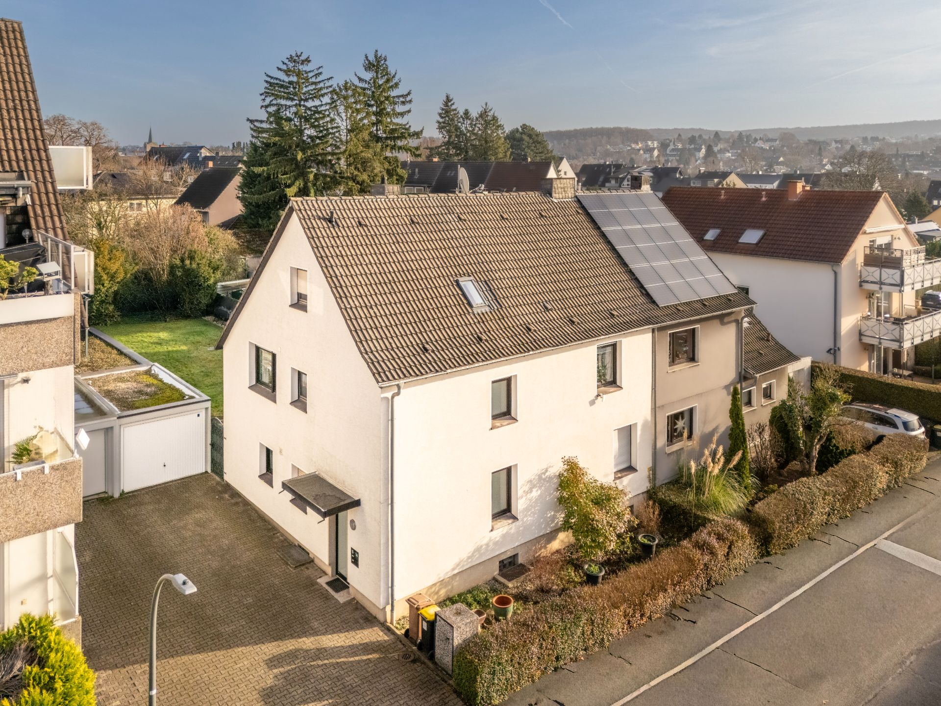Zweistöckiges, weißes Wohnhaus mit Solarpanelen auf dem Dach und Vorgarten, Ansicht von oben.