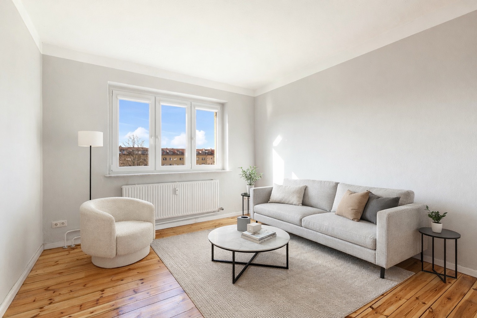 Helles Wohnzimmer mit grauem Sofa, Sessel, Couchtisch, Teppich und Fenster.