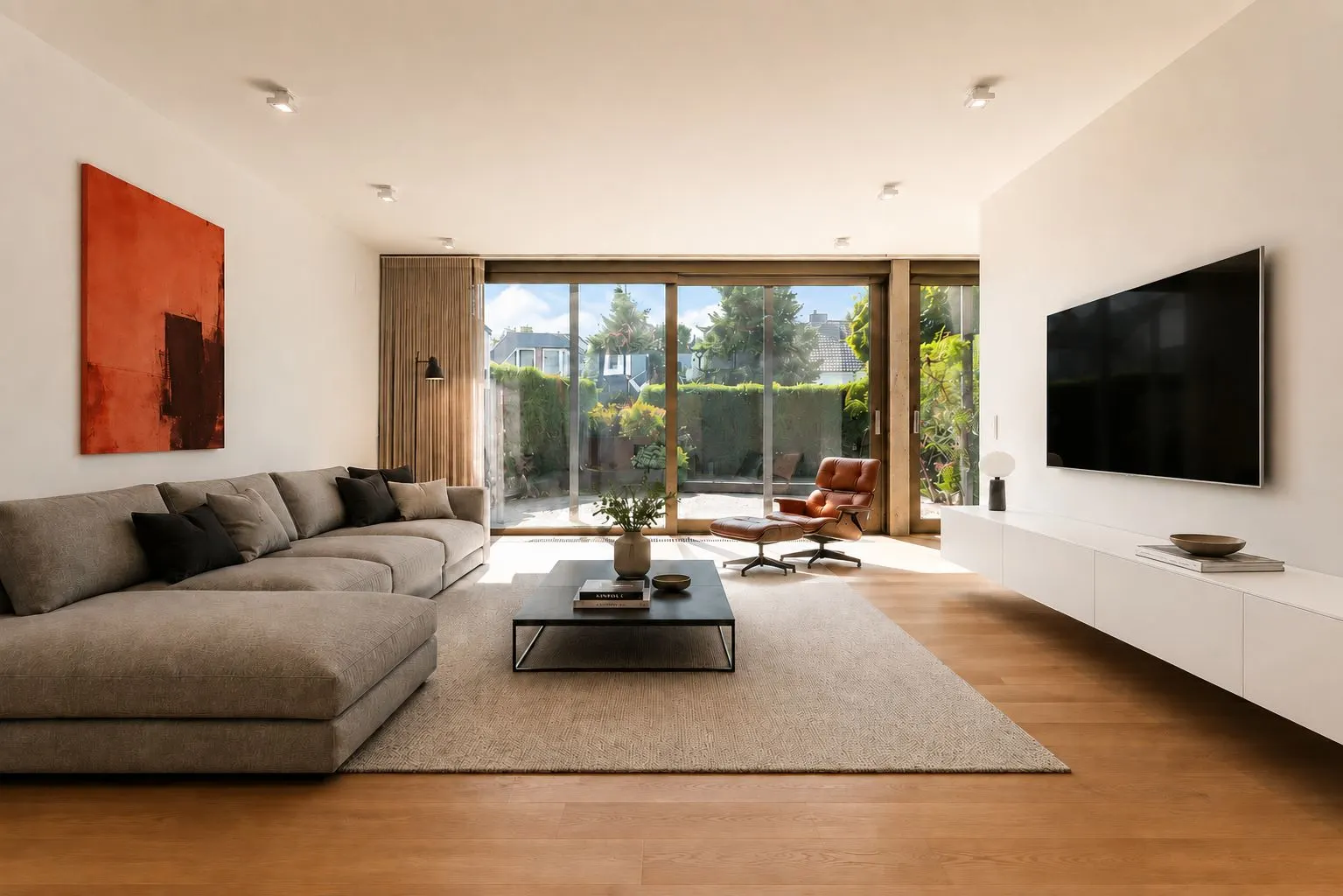 Helles Wohnzimmer mit grauem Sofa, Couchtisch, Sessel, großem Fenster und Wandfernseher.
