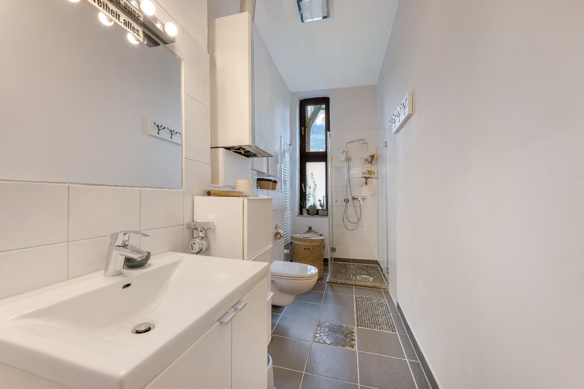 Modernes Badezimmer mit Waschbecken, Spiegel, Toilette und ebenerdiger Dusche.