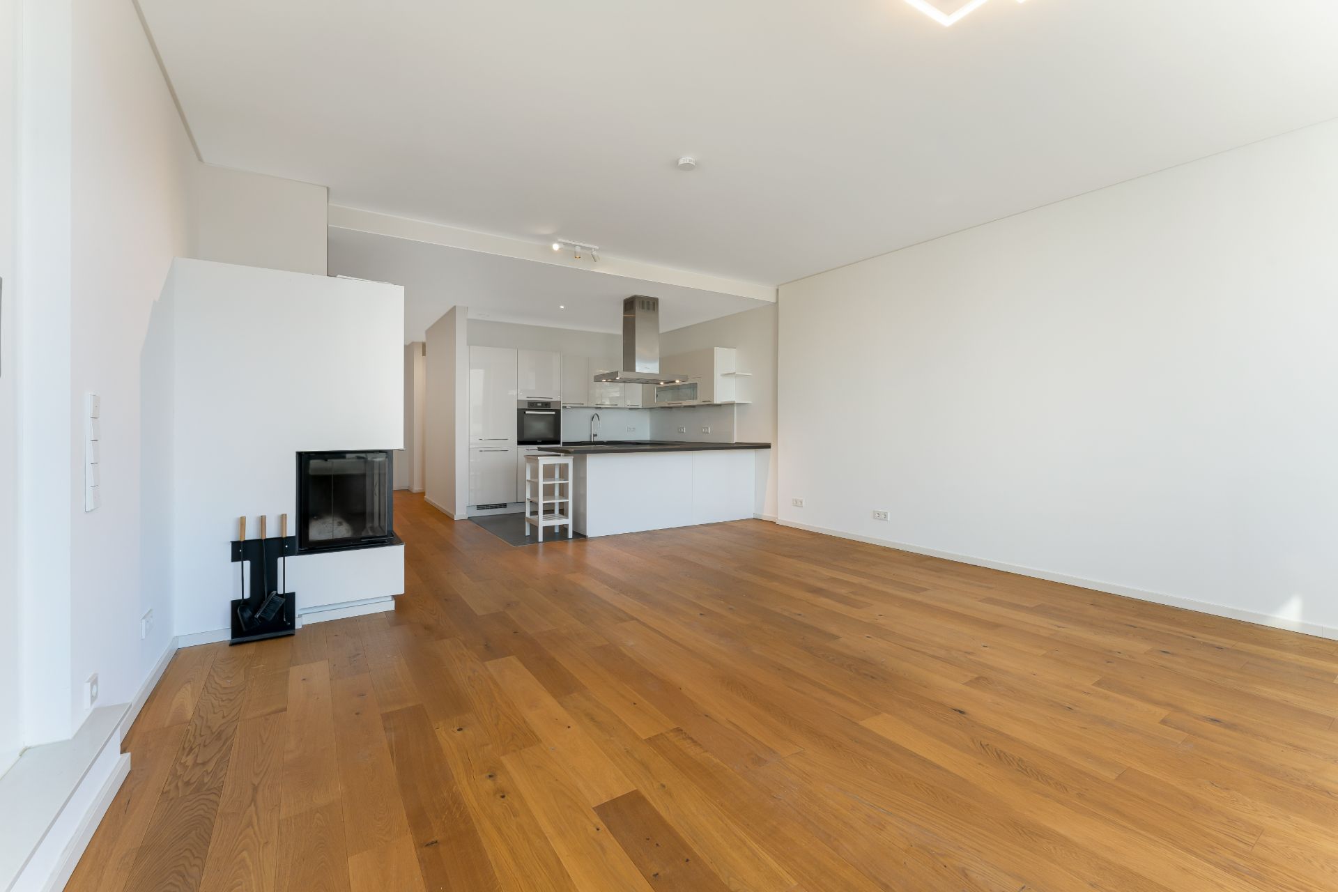 Helles Wohnzimmer mit Holzboden, offener Küche und Kamin.