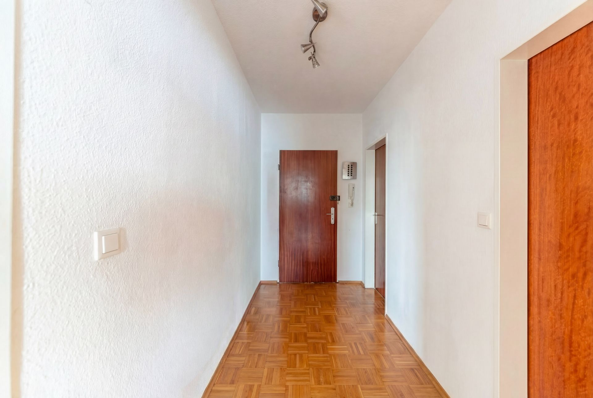 Heller Flur mit Parkettboden, weißen Wänden und Holztüren in einer Wohnung.