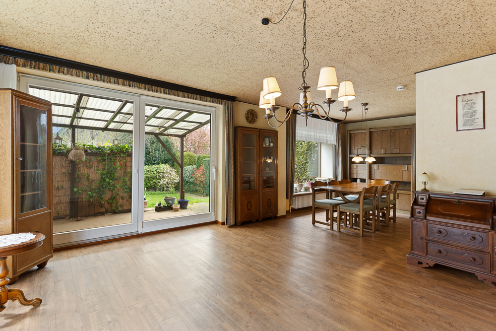 Großes Wohnzimmer mit Holzmöbeln, Esstisch und Blick auf eine überdachte Terrasse und Garten.