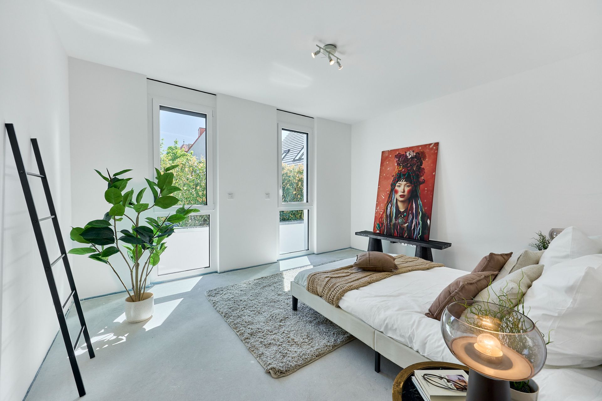 Helles Schlafzimmer mit Doppelbett, großem Fenster, Pflanze und Bild an der Wand.