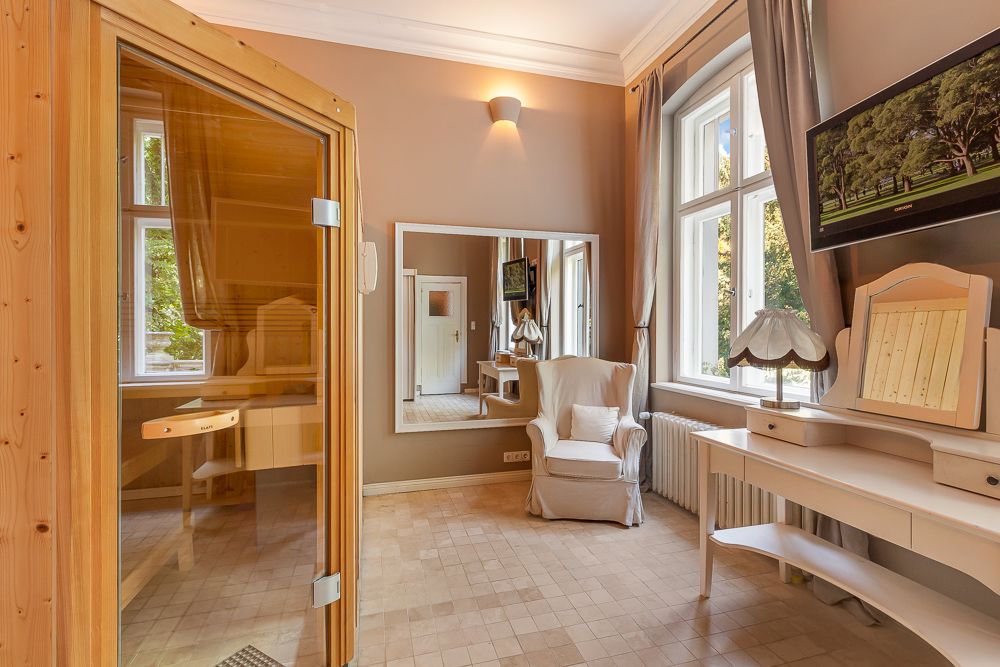 Heller Raum mit Sauna, Sessel, Schminktisch, großen Fenstern und Wandspiegel.