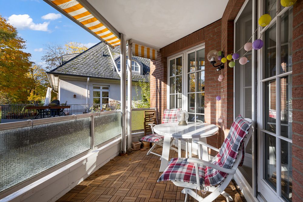 Überdachter Balkon mit zwei Stühlen, rundem Tisch und gestreifter Markise.
