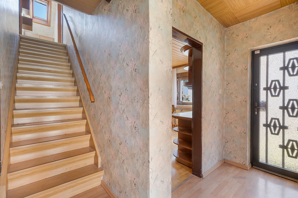 Flur mit Holztreppe, floral gemusterten Wänden und Glastür mit Gittermuster.