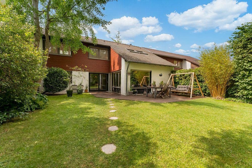 Garten mit Rasen, Terrasse, Sitzgruppe und Schaukel vor einem modernen Wohnhaus.