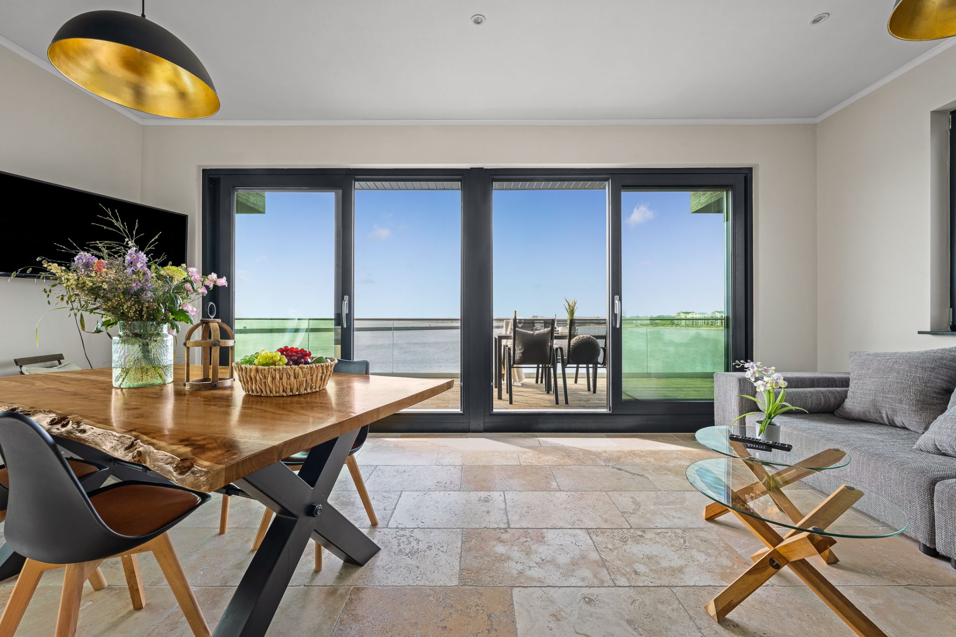 Helles Wohnzimmer mit Esstisch, Sofa und Zugang zu einem Balkon mit Sitzbereich.
