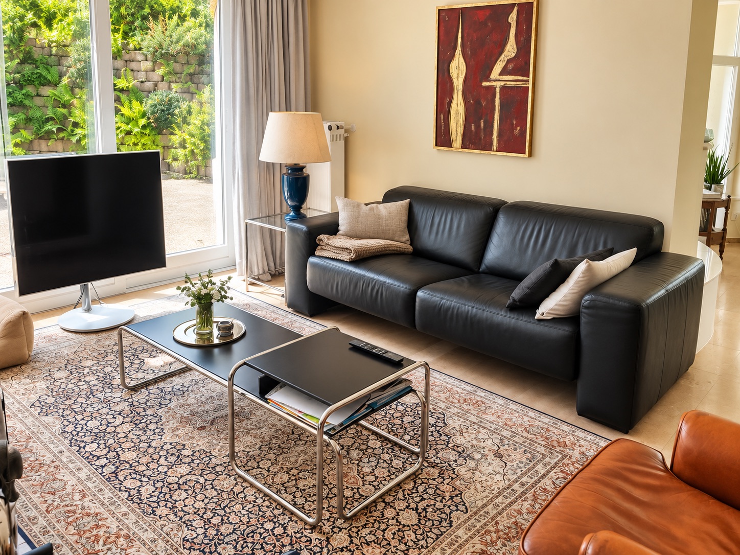 Modernes Wohnzimmer mit schwarzem Sofa, Teppich, Couchtisch, Fernseher und großem Fenster.