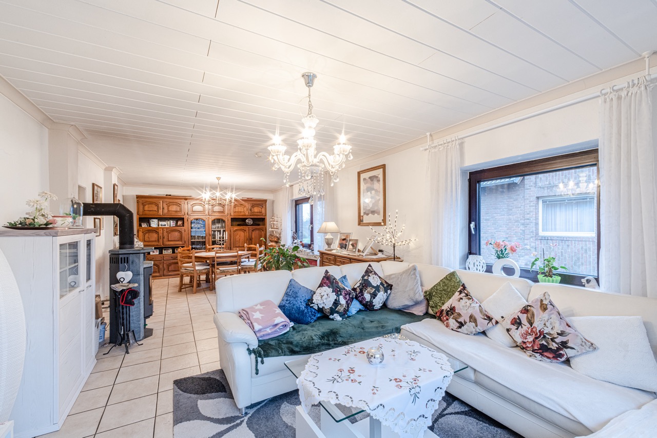 Helles Wohnzimmer mit weißem Ecksofa, bunten Kissen, Kamin, Esstisch und Kronleuchtern.