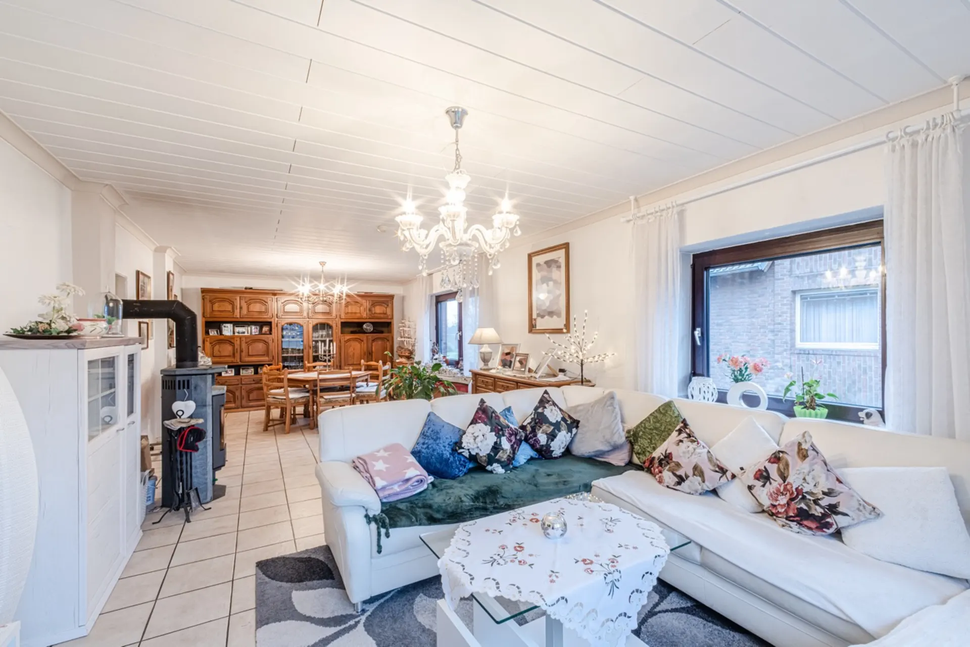 Helles Wohnzimmer mit weißem Ecksofa, bunten Kissen, Kamin, Esstisch und Kronleuchtern.