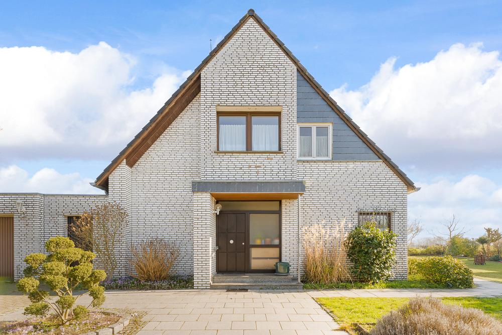 Vorderansicht eines modernen Einfamilienhauses mit weißer Klinkerfassade und Garten.