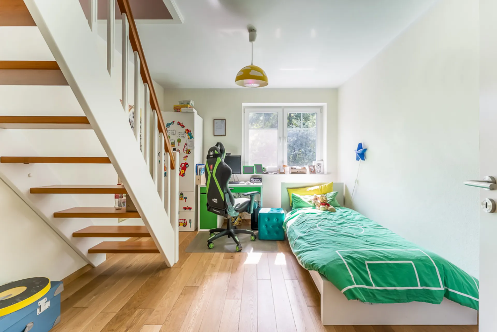 Helles Kinderzimmer mit Einzelbett, Schreibtisch, Stuhl und Treppe, Holzboden.