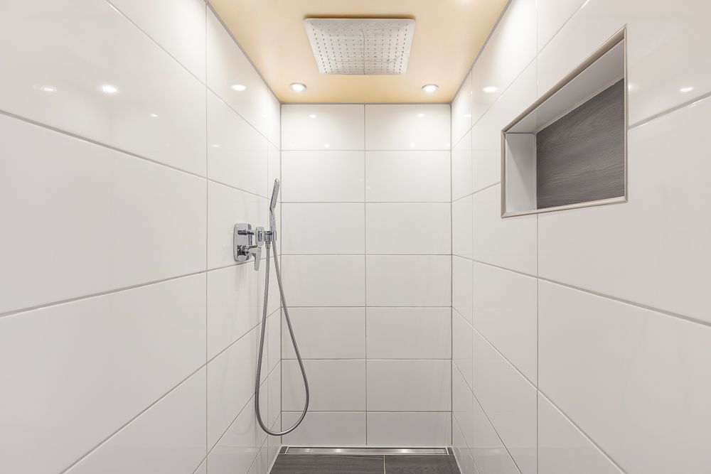 Moderne, geflieste Dusche mit Regenduschkopf, Handbrause und Wandnische.