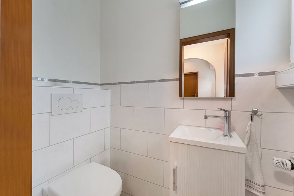 Kleines Badezimmer mit WC, Waschbecken, Spiegel und weiß gefliesten Wänden.