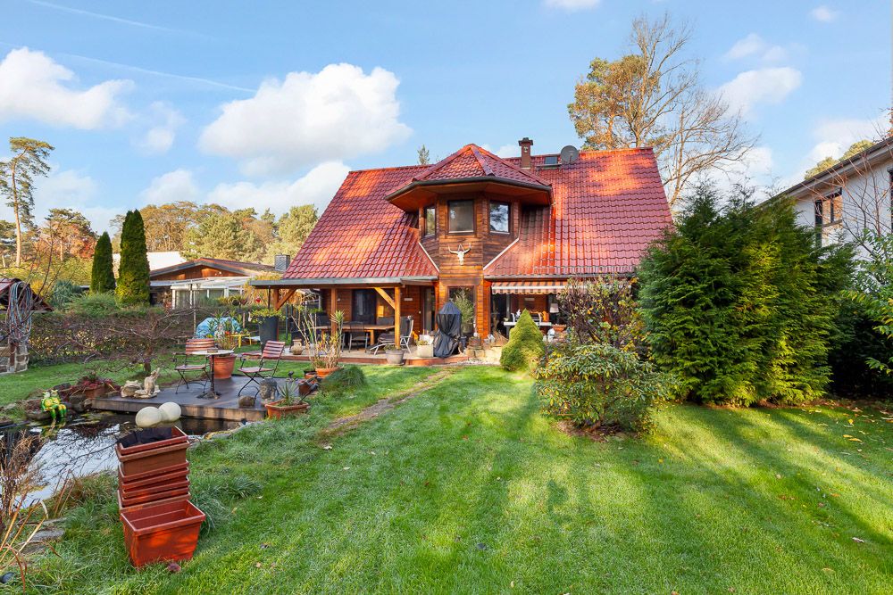 Holzhaus mit rotem Dach, Garten und Teich im Vordergrund.