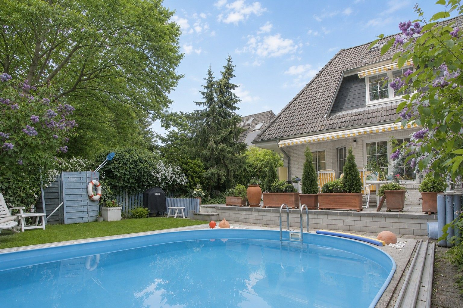 Garten mit rundem Pool, Liegestuhl, Grill und Haus mit Terrasse im Hintergrund.