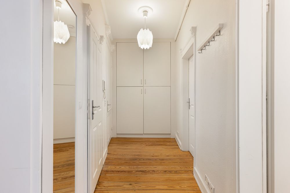 Heller Flur mit Holzfußboden, weißen Wänden, Garderobenhaken und Einbauschrank.