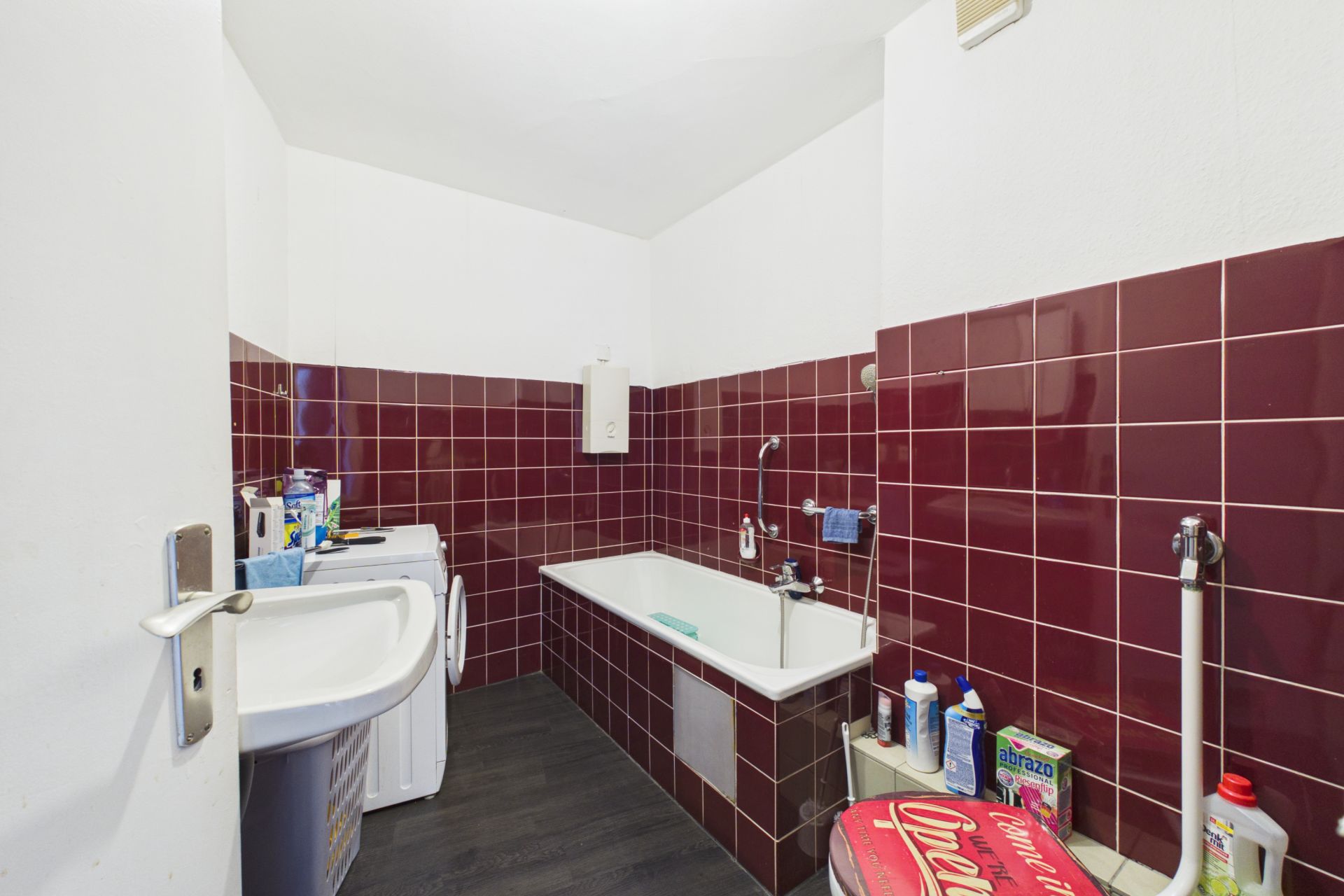 Badezimmer mit Badewanne, Waschbecken, Waschmaschine und roten Wandfliesen.