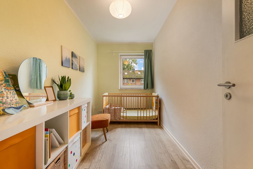 Helles Kinderzimmer mit Holzbett, Regal, Hocker und Fenster mit Blick nach draußen.