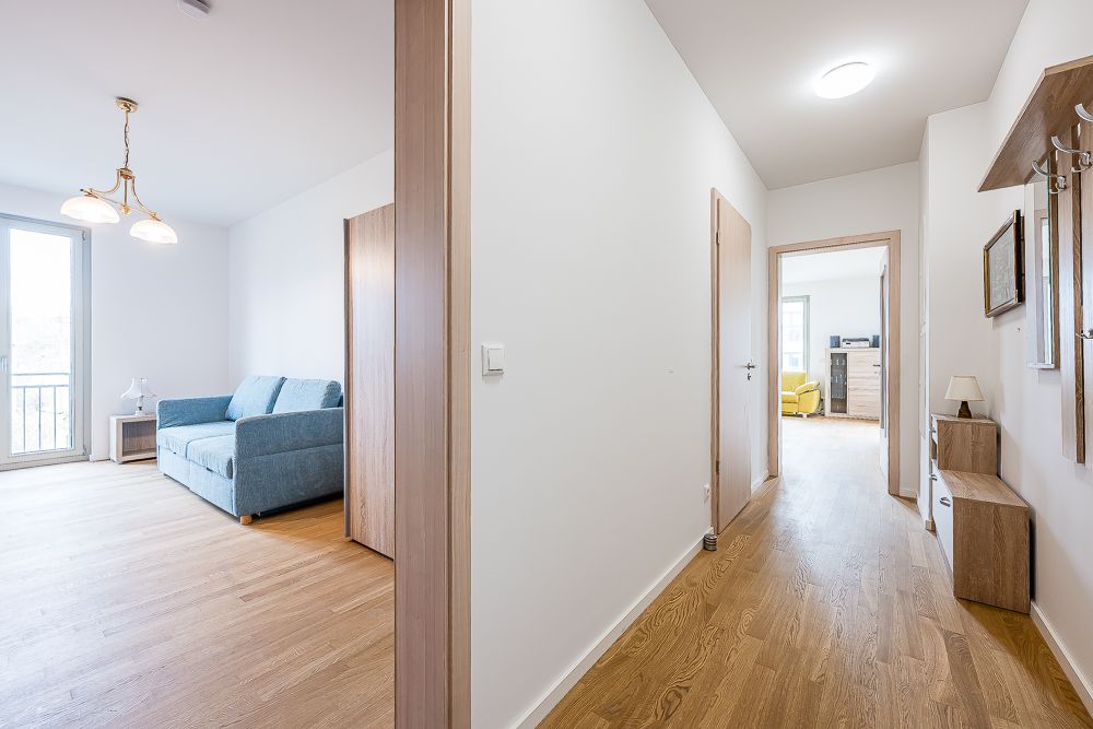Heller Flur mit Holzboden, links ein Zimmer mit Sofa, geradeaus Raum mit gelbem Sessel.