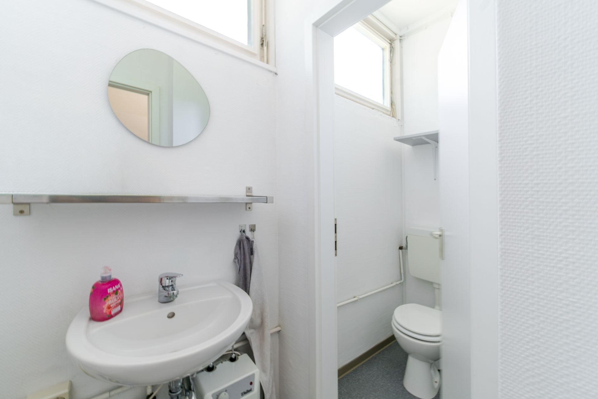 Kleines Badezimmer mit Waschbecken, Spiegel und separater Toilette.