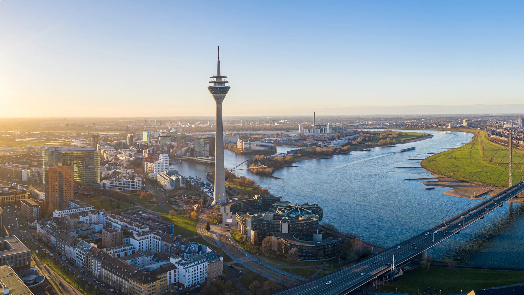 Panoramaaufnahme einer Stadt mit Fluss, Brücke und hohem Fernsehturm.