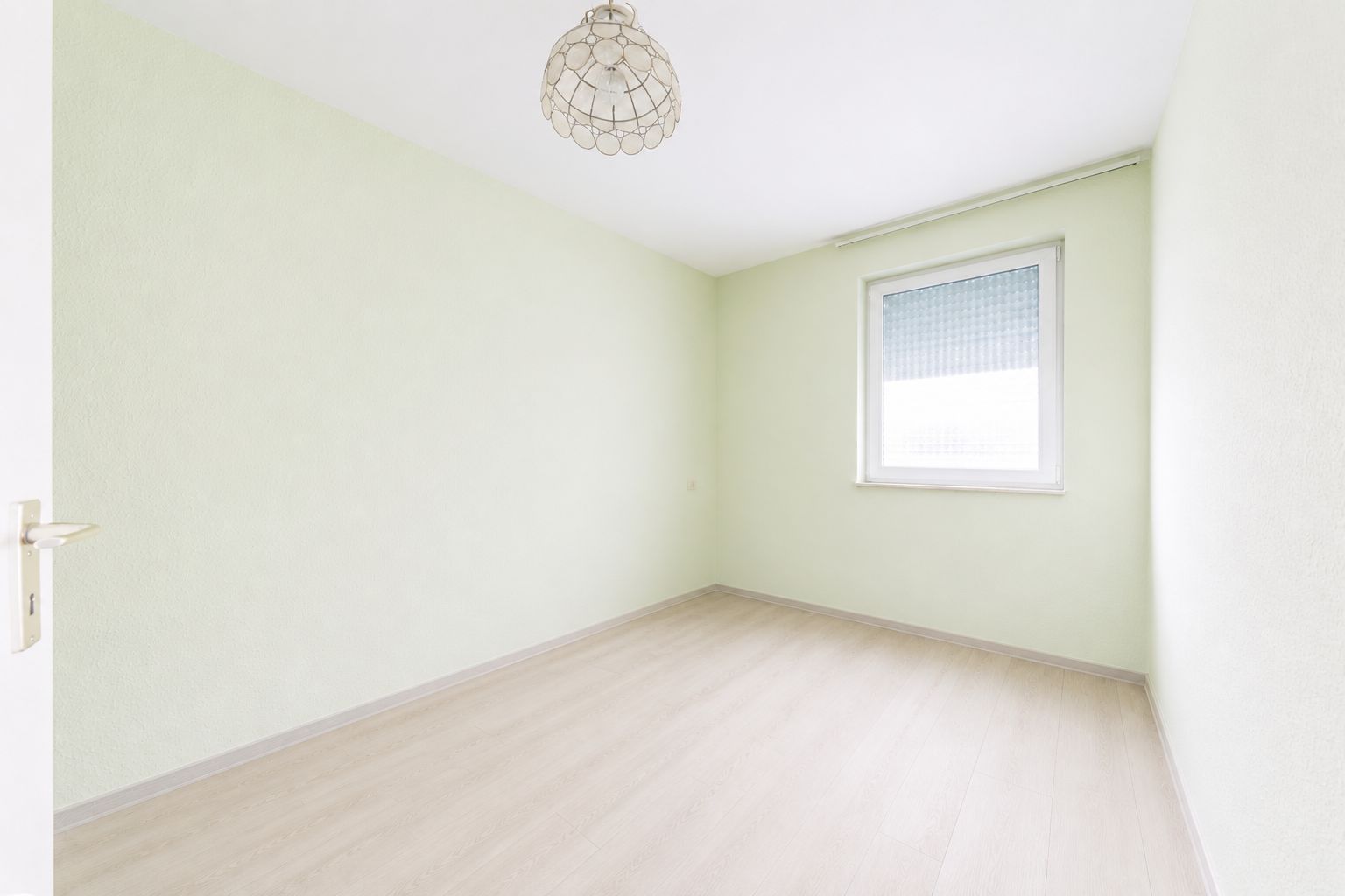 Helles, leeres Zimmer mit hellem Holzboden, Fenster und Lampe an der Decke.