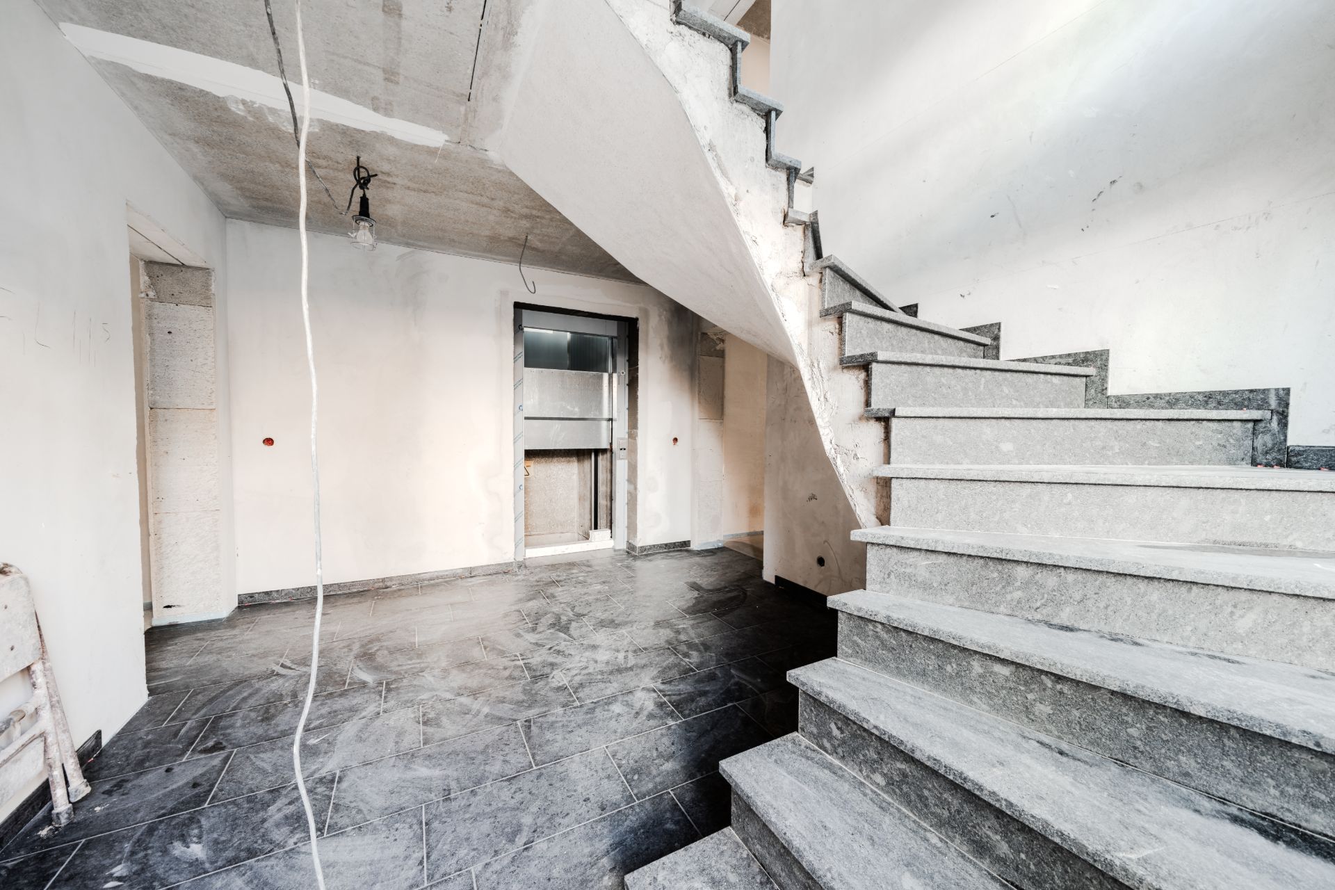 Innenbereich eines Hauses mit unbeendeter Treppe und grauem Fliesenboden.
