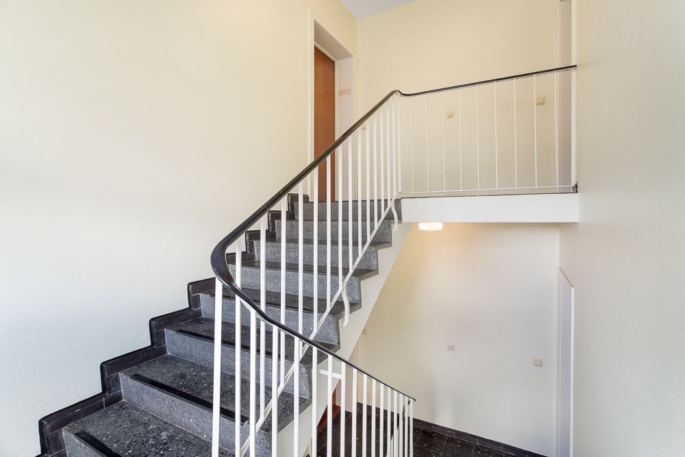 Treppenhaus mit grauen Stufen, weißen Wänden und Metallgeländer in einem Wohnhaus.