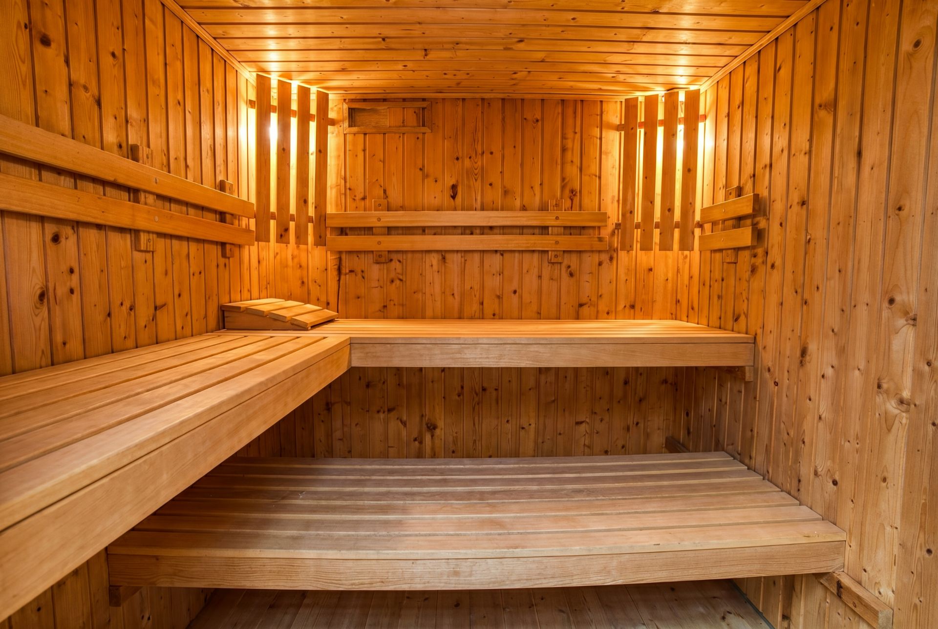 Holzsauna mit zwei Sitzbänken und warmem Licht an den Wänden.