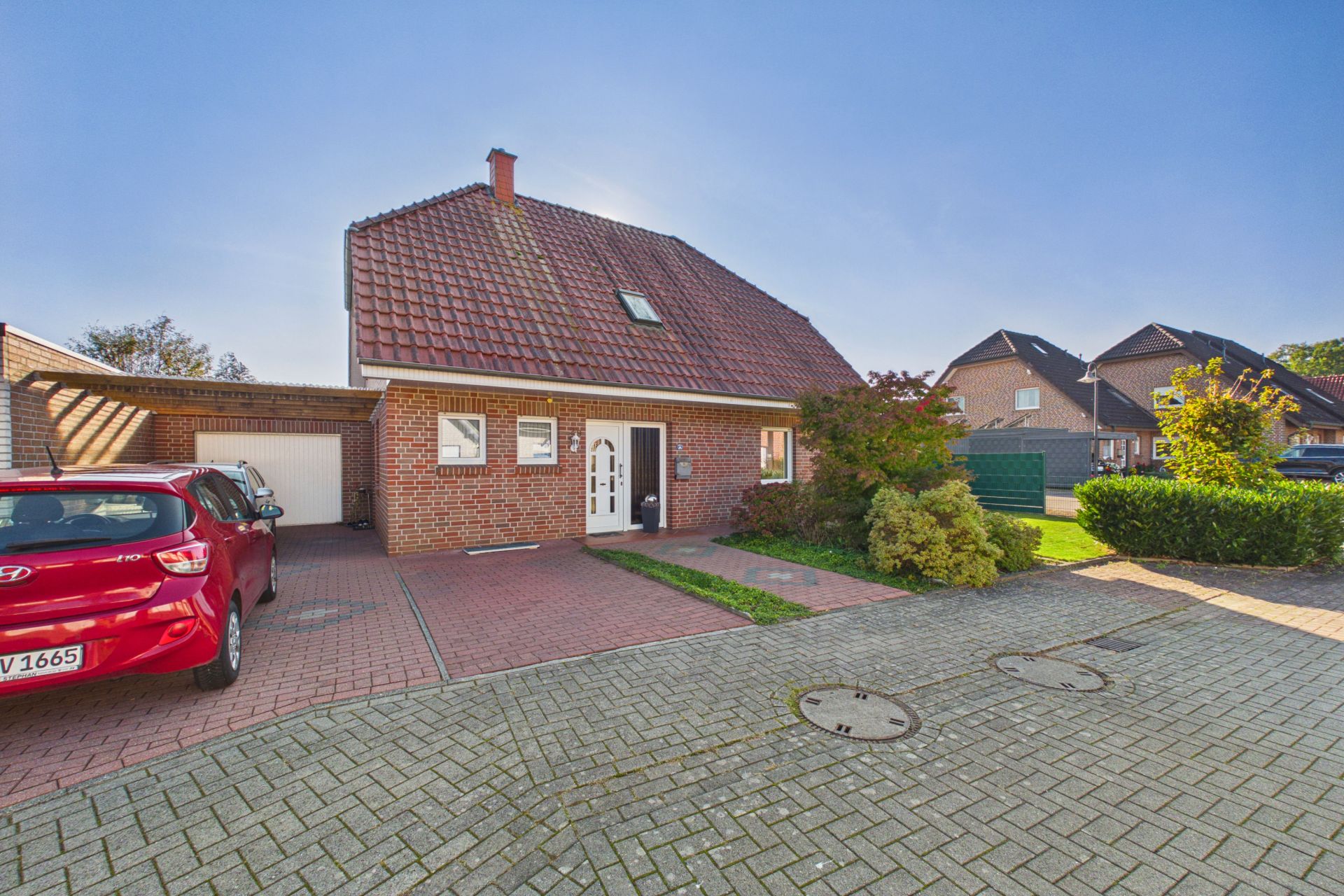 Einfamilienhaus aus rotem Backstein mit Satteldach, Auffahrt, rotem Auto und Garten.