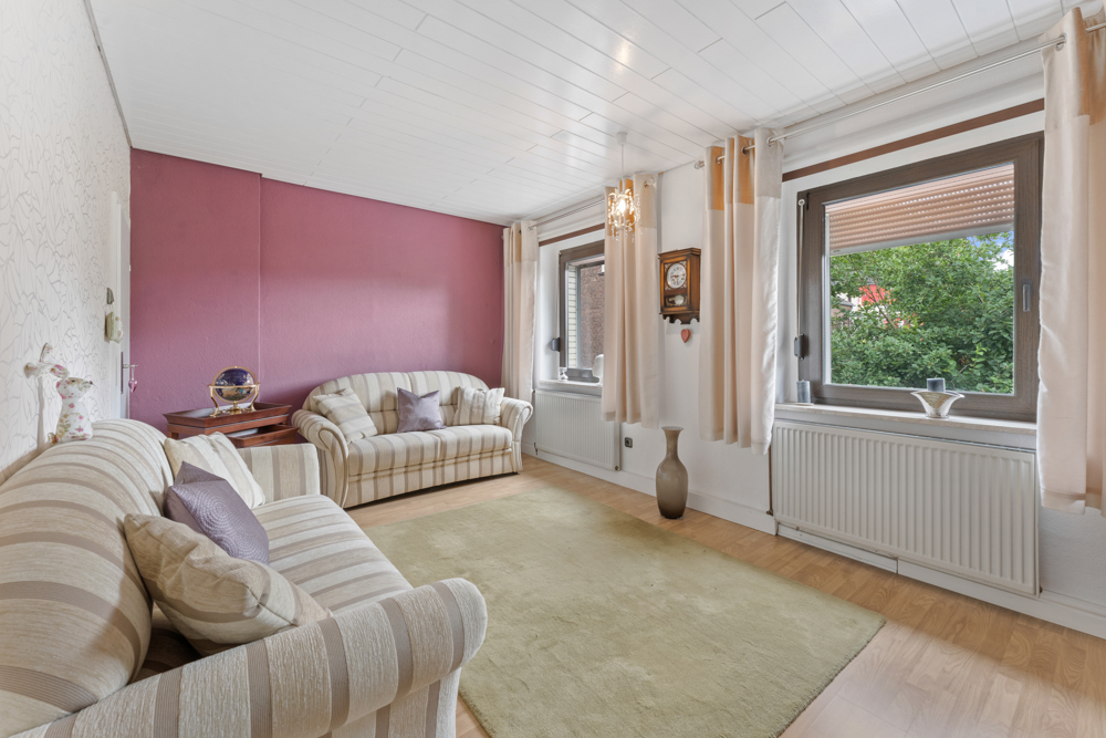 Wohnzimmer mit zwei gestreiften Sofas, großem Teppich und zwei Fenstern mit Vorhängen.
