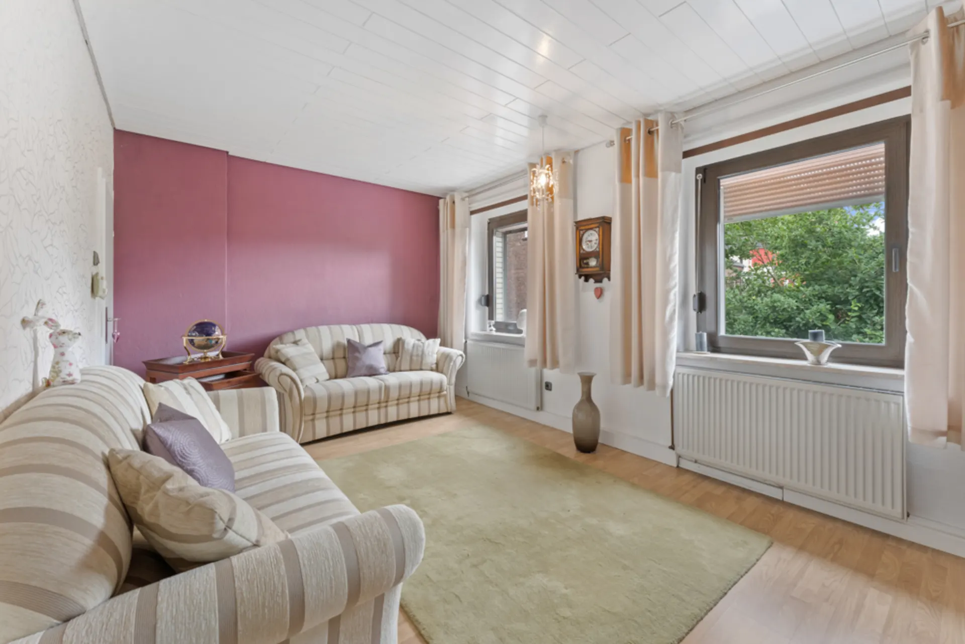 Wohnzimmer mit zwei gestreiften Sofas, großem Teppich und zwei Fenstern mit Vorhängen.