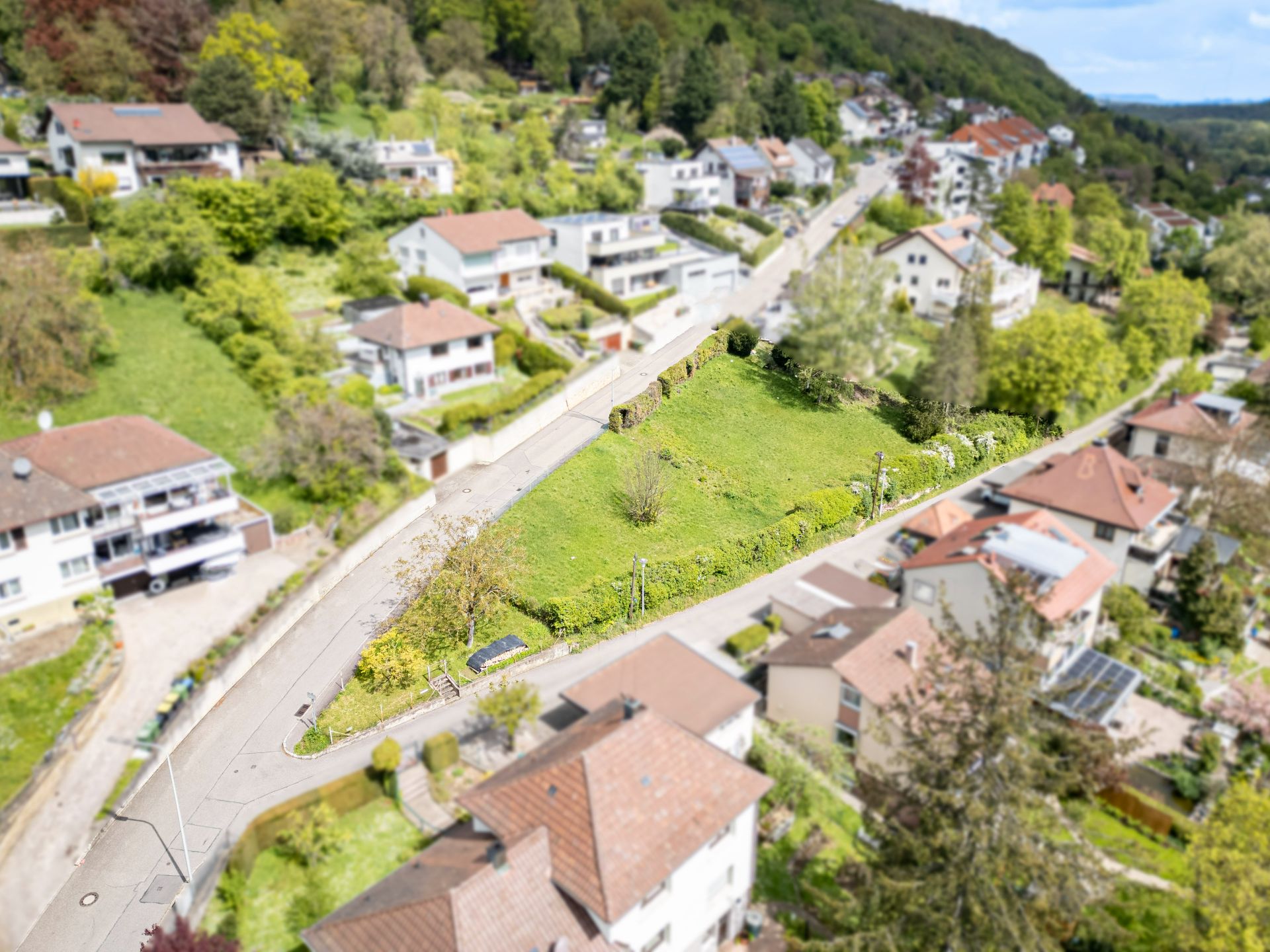 Luftaufnahme eines Wohnviertels mit Häusern, Straßen und einer grasbewachsenen freien Fläche.