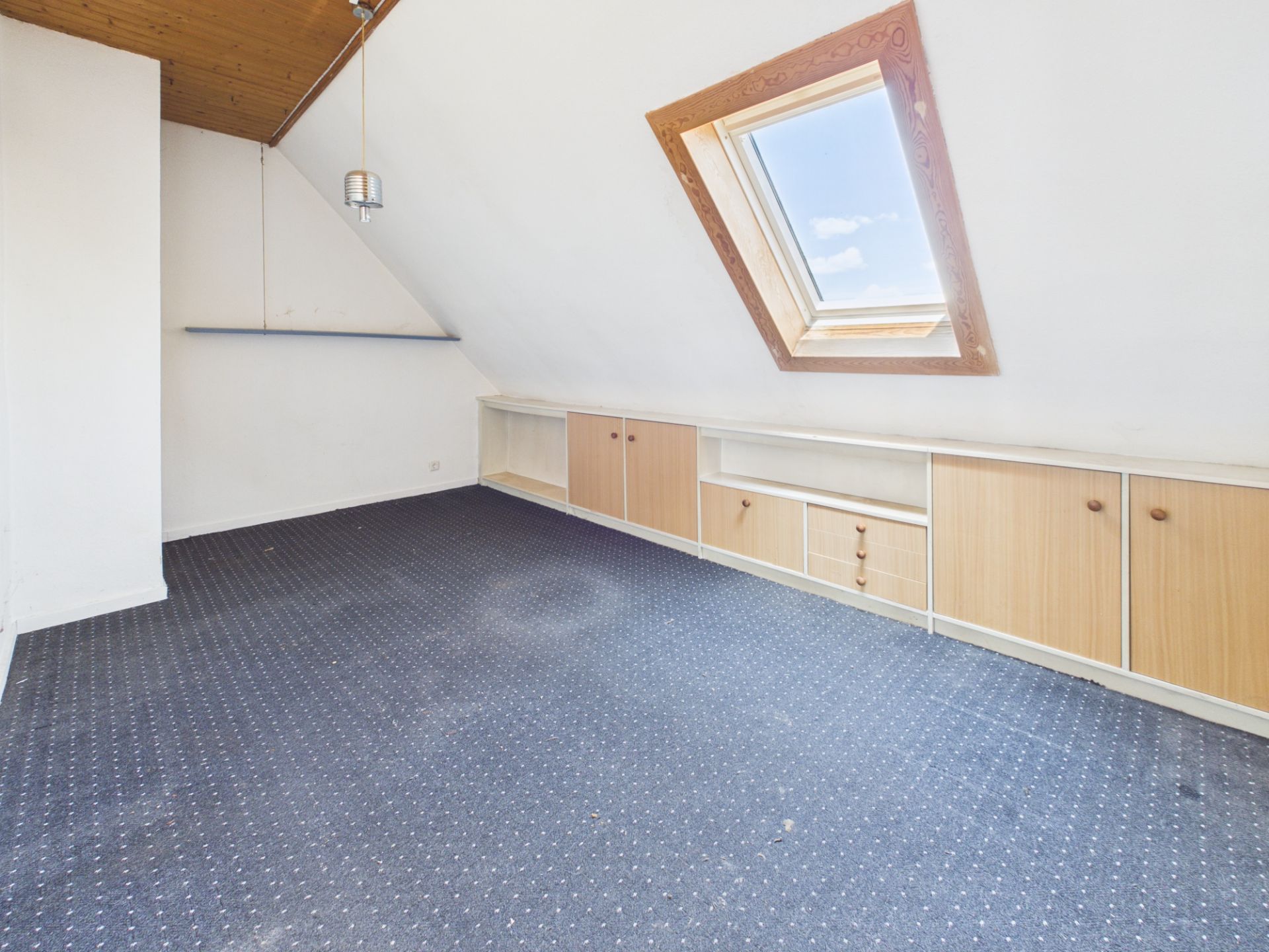 Dachzimmer mit Teppichboden, Einbauschränken und großem Dachfenster.