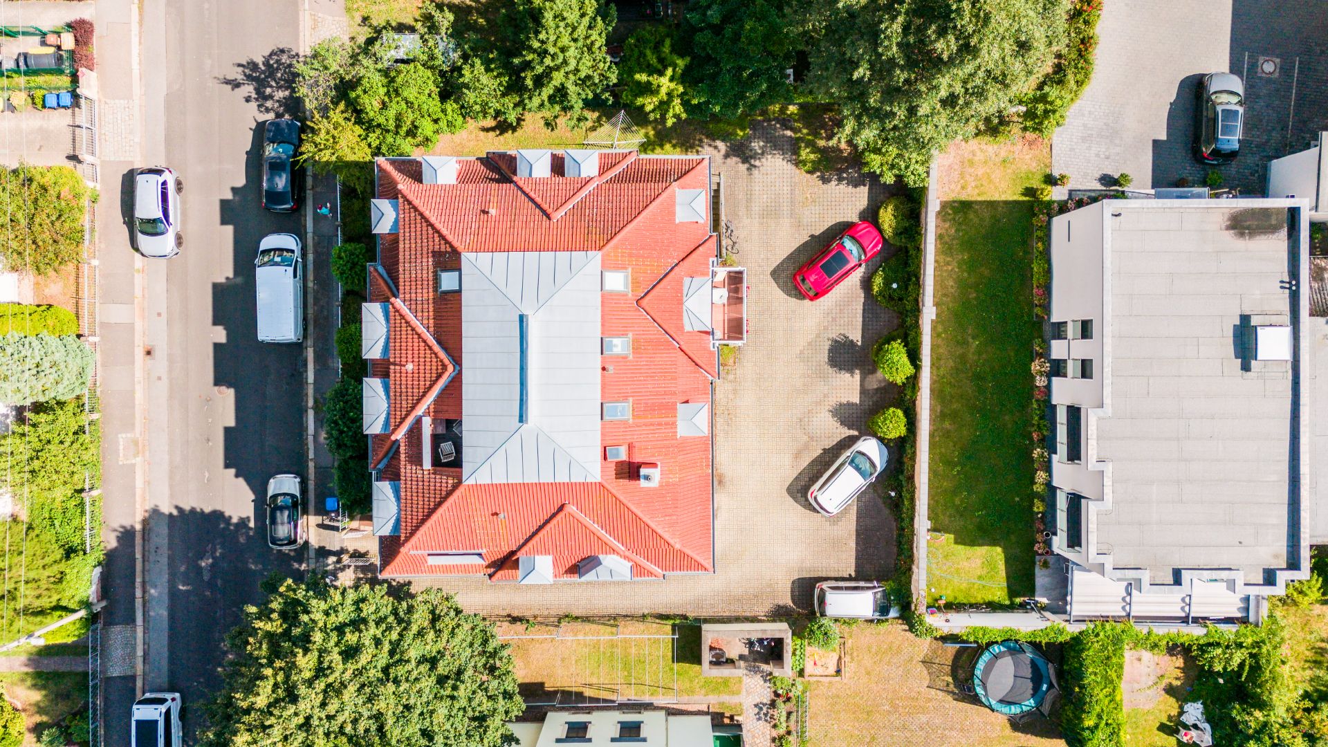 Luftaufnahme eines Hauses mit rotem Dach und umliegenden Autos und Gärten.