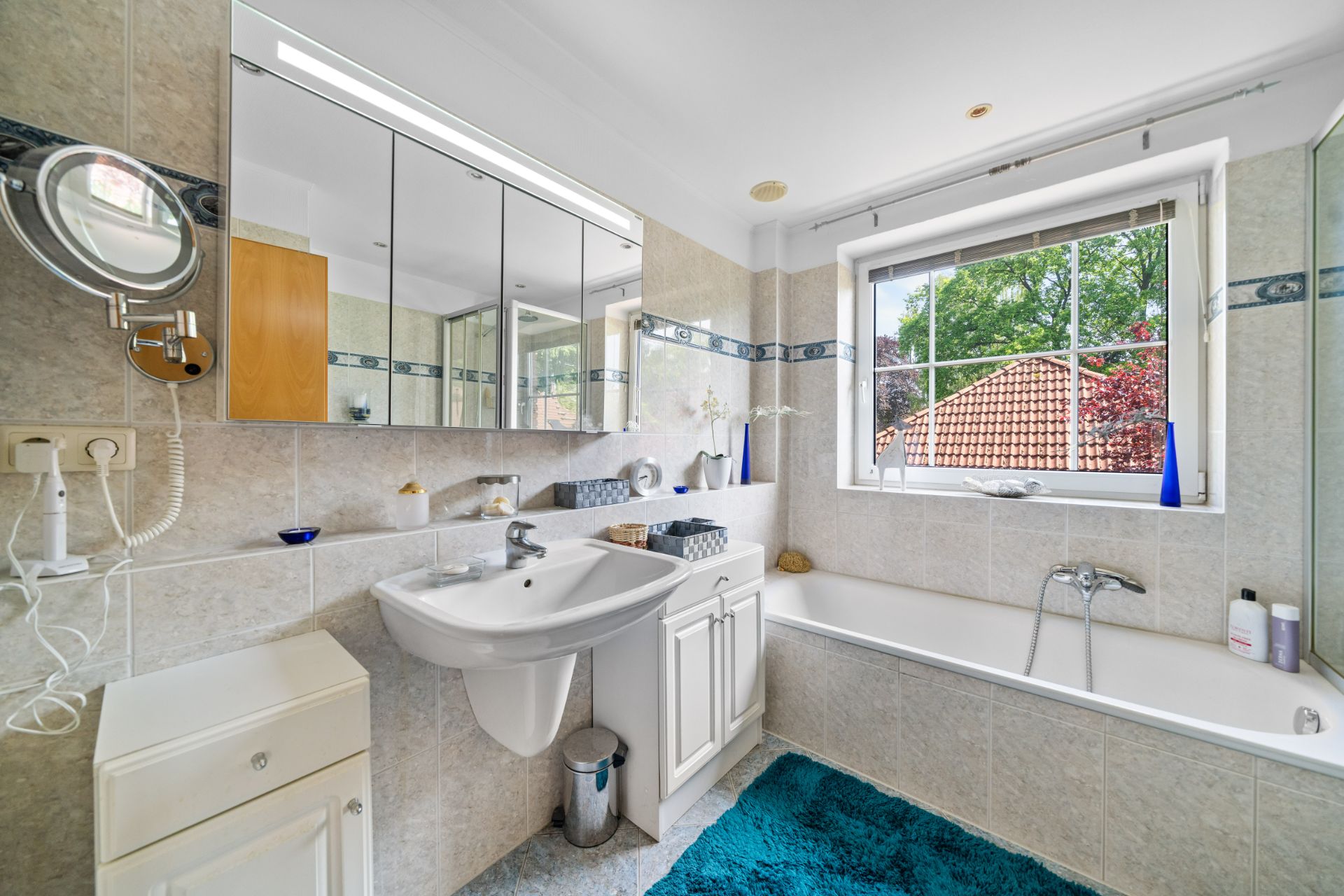 Modernes Badezimmer mit Waschbecken, Badewanne, Spiegel und Fenster mit Blick nach draußen.