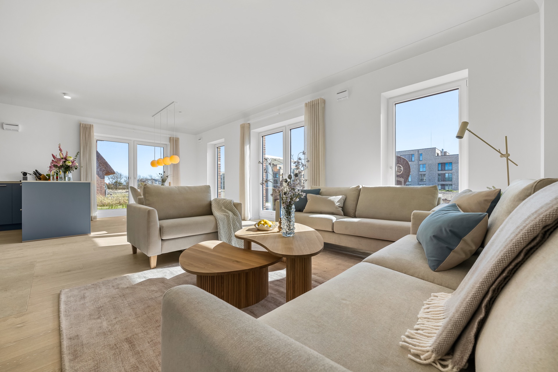 Helles Wohnzimmer mit beigen Sofas, Holztischen und großen Fenstern.