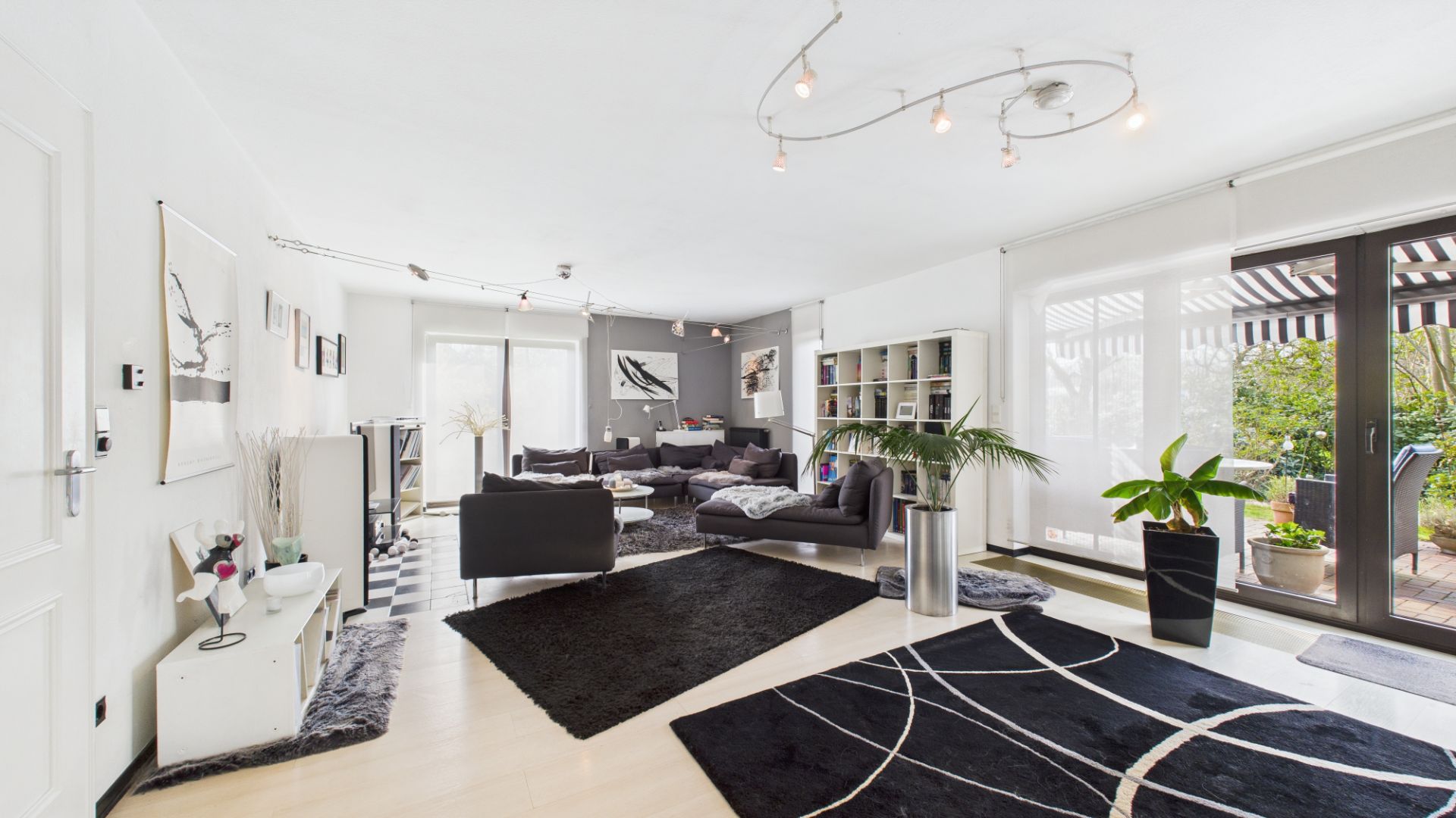 Helles Wohnzimmer mit modernen Möbeln, großen Fenstern, Teppichen und Pflanzen.