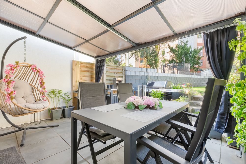Überdachte Terrasse mit Esstisch, Stühlen, Hängesessel und Pflanzen, Blick in den Garten.