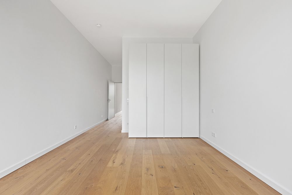 Leerer Raum mit Holzfußboden, weißen Wänden und großem weißen Einbauschrank.