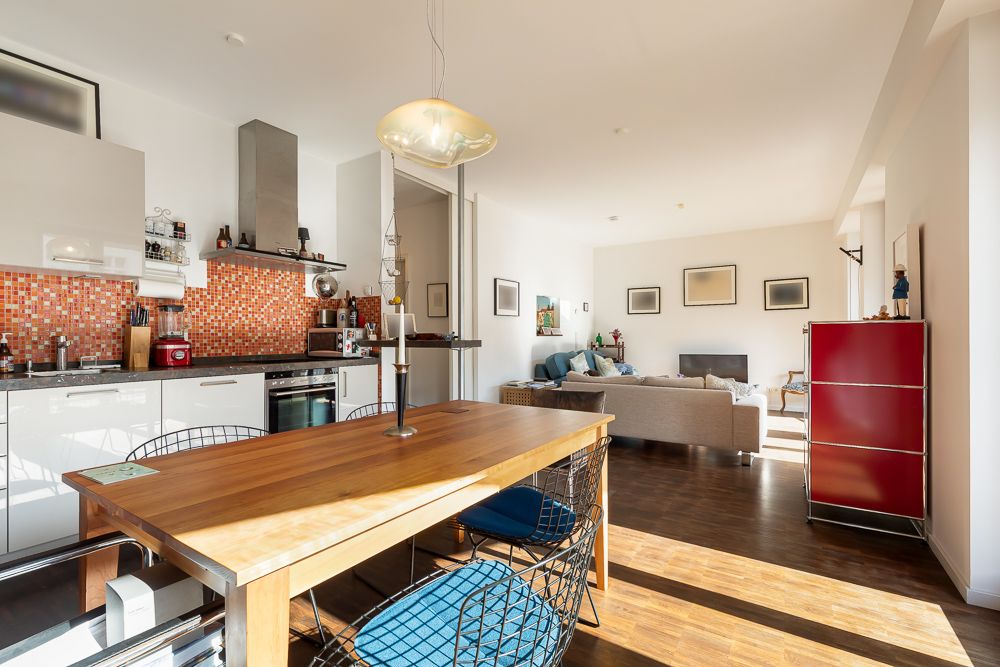 Helle Wohnküche mit Esstisch, offener Küche, Sofa und roten Schränken im Hintergrund.