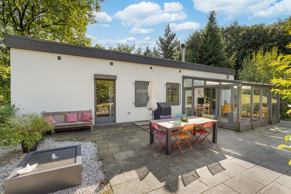 Moderne Terrasse mit buntem Esstisch, Sitzbank und Wintergarten an weißem Haus.