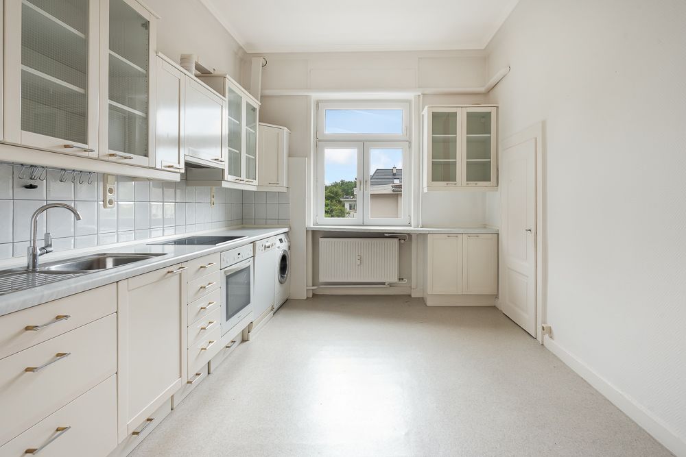 Helle Küche mit weißen Schränken, Herd, Spüle und großem Fenster.