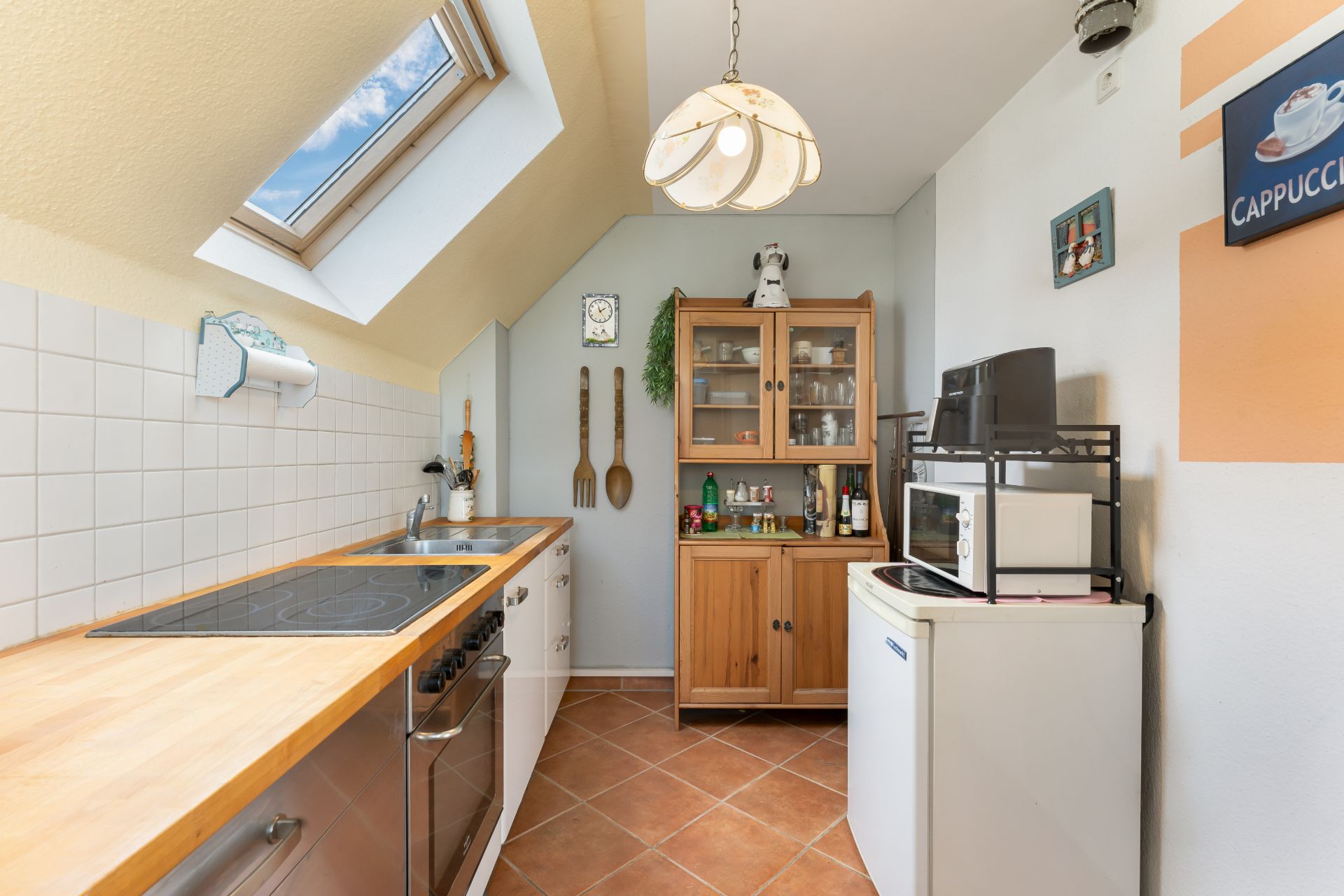 Helle Küche mit Dachfenster, Holzarbeitsplatte, Herd, Schrank und kleinem Kühlschrank.
