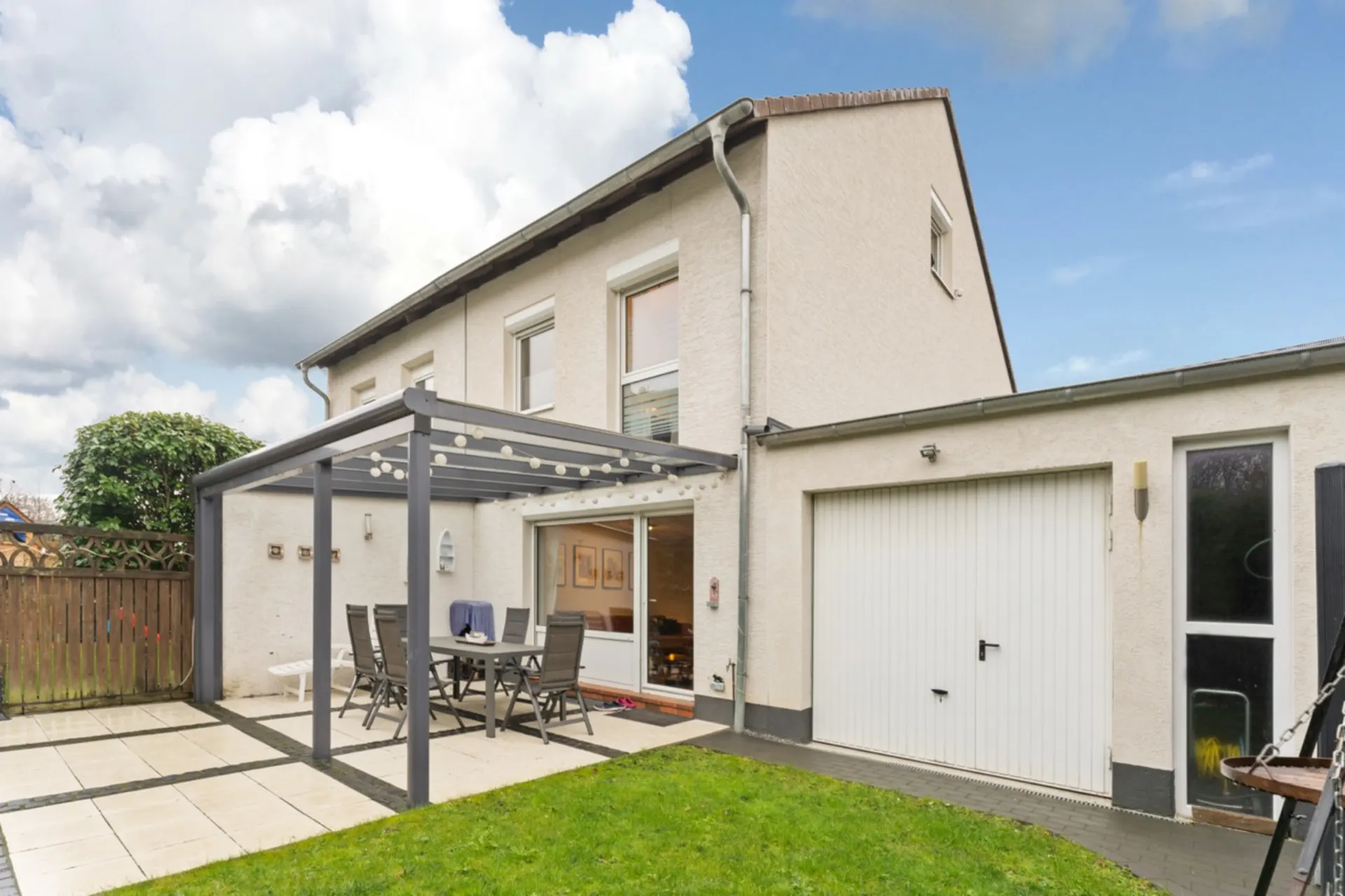 Helles Wohnhaus mit Terrasse, Pergola, Gartenmöbeln und angrenzender Garage.
