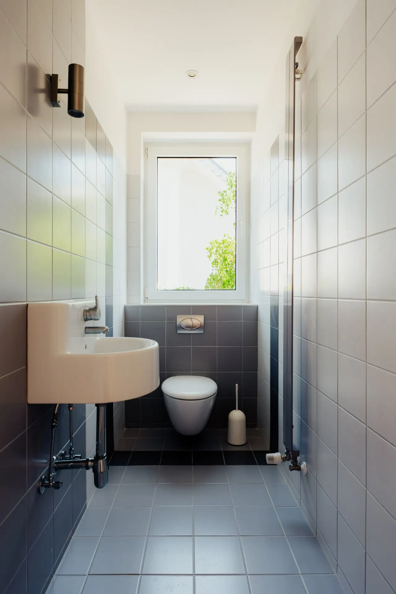 Modernes, schmales Bad mit WC, Waschbecken, Wandheizung und Fenster.