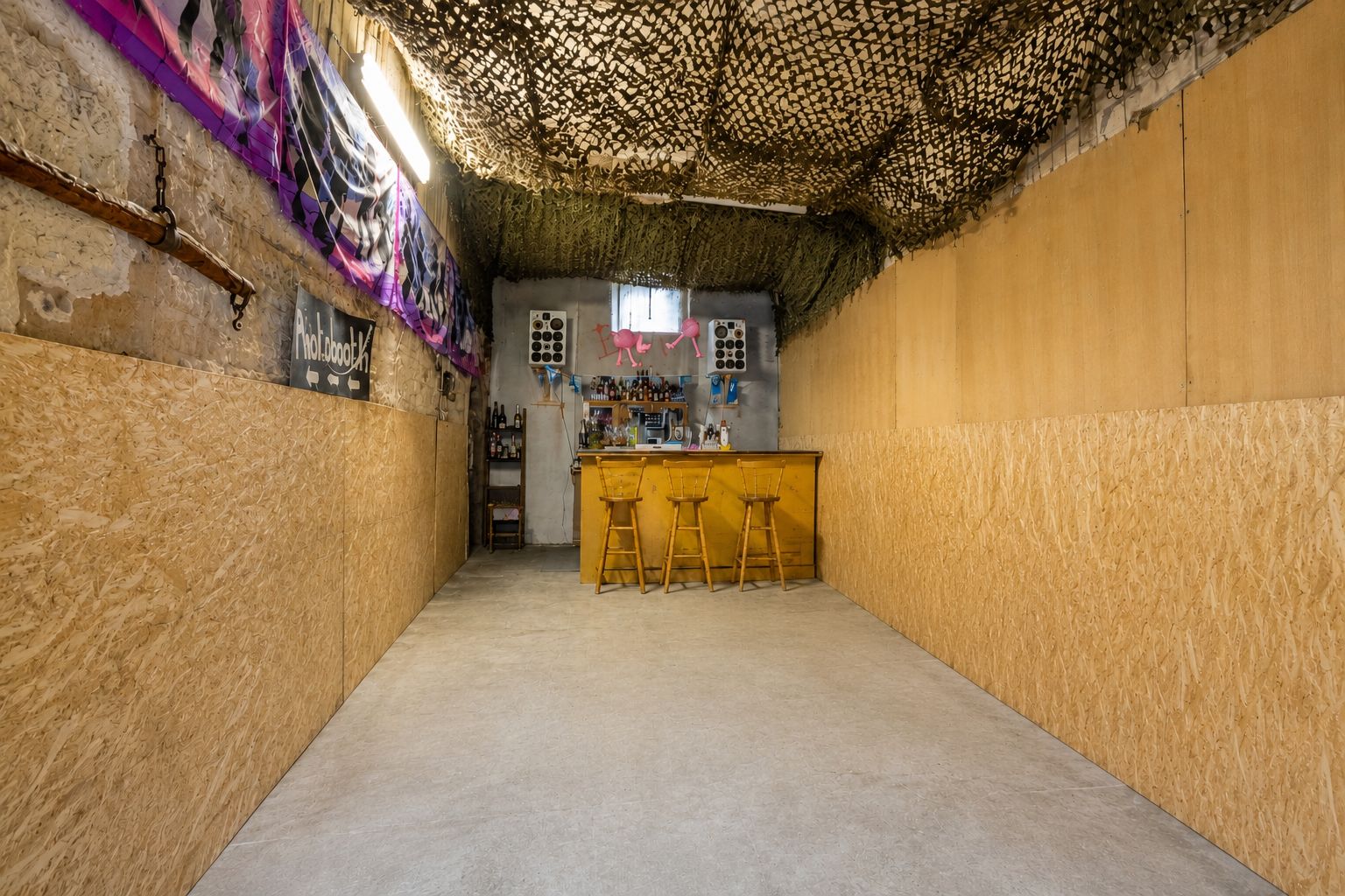 Langer Raum mit Holztheke, drei Hockern und dekorativem Netz an der Decke.